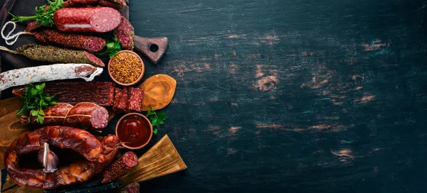 Salam ve aperatifler ürün yelpazesine. Sosis Amandine, sosis, salam, paperoni. Siyah ahşap arka plan üzerinde. Üstten görünüm. Metniniz için boş alan.