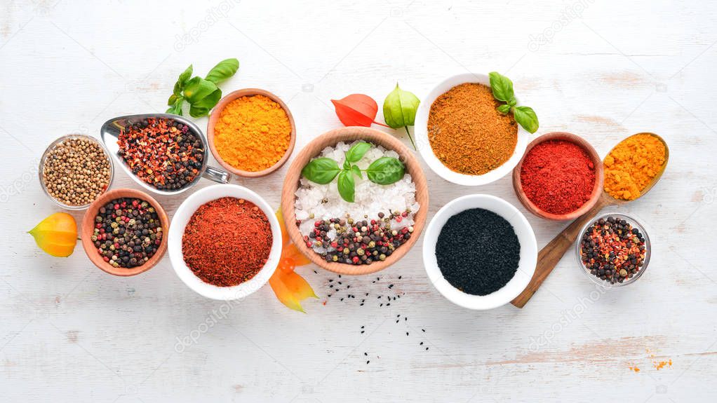 A set of Spices and herbs on a white wooden table. Basil, pepper, saffron, spices. Indian traditional cuisine. Top view. Free copy space.