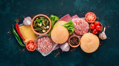 Burger hazırlanması. Eti, domates, soğan. Siyah taş arka plan üzerinde. Üstten görünüm. Ücretsiz kopya alanı.