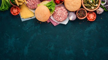 Burger hazırlanması. Eti, domates, soğan. Siyah taş arka plan üzerinde. Üstten görünüm. Ücretsiz kopya alanı.