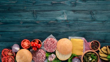 Burger hazırlanması. Eti, domates, soğan. Mavi ahşap arka plan üzerinde. Üstten görünüm. Ücretsiz kopya alanı.