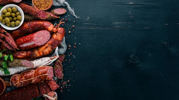 Salam ve aperatifler ürün yelpazesine. Sosis Amandine, sosis, salam, paperoni. Siyah ahşap arka plan üzerinde. Üstten görünüm. Metniniz için boş alan.