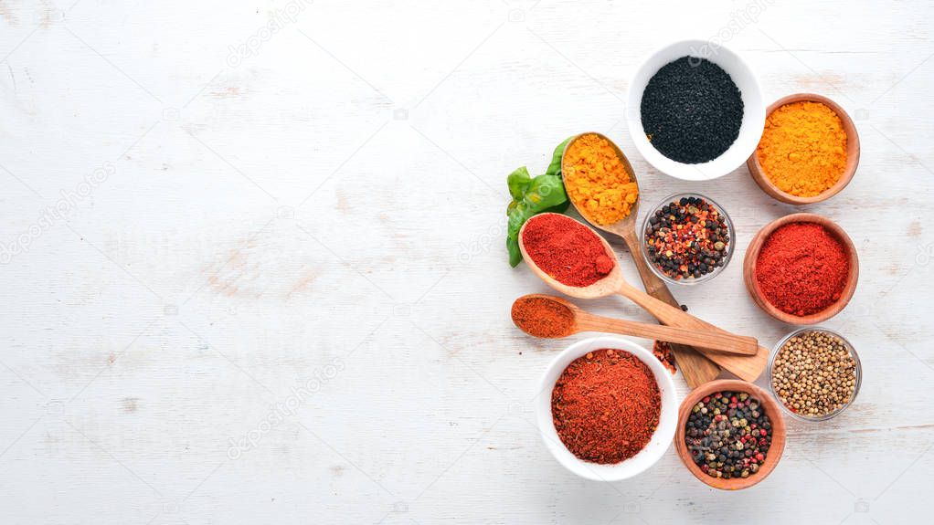 A set of Spices and herbs on a white wooden table. Basil, pepper, saffron, spices. Indian traditional cuisine. Top view. Free copy space.