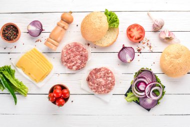 Burger hazırlanması. Eti, domates, soğan. Beyaz ahşap zemin üzerinde. Üstten görünüm. Ücretsiz kopya alanı.