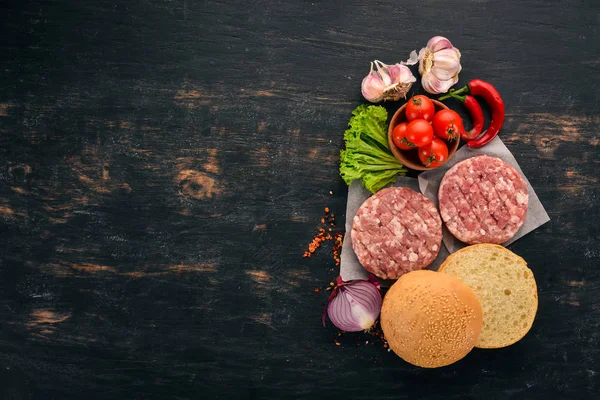 Raw burger Cooking a burger with meat. On a black wooden background. Top view. Free copy space.