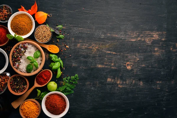 A set of spices and herbs. Indian cuisine. Pepper, salt, paprika, basil, turmeric. On a black wooden chalkboard. Top view. Free copy space.