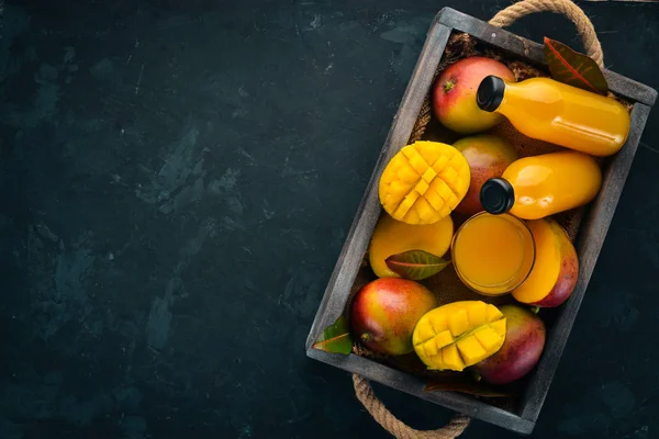 Mango and juice in a wooden box. On a wooden background. Tropical Fruits. Top view. Free copy space.