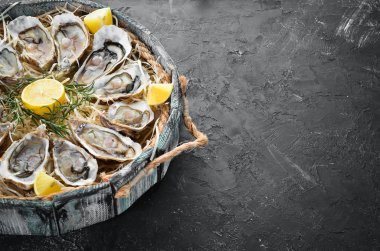 Ahşap kutuda limon ile taze istiridye. Siyah taş arka planda. Üst görünüm. Ücretsiz kopya alanı.