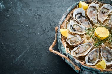 Ahşap kutuda limon ile taze istiridye. Siyah taş arka planda. Üst görünüm. Ücretsiz kopya alanı.