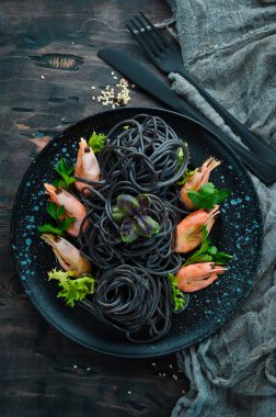 Siyah bir tabak karides ile siyah makarna. Üstten Görünüm. Beyaz ahşap zemin üzerinde. Ücretsiz kopya alanı.