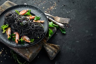 Siyah bir tabak karides ile siyah makarna. Üstten Görünüm. Beyaz ahşap zemin üzerinde. Ücretsiz kopya alanı.