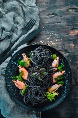 Siyah bir tabak karides ile siyah makarna. Üstten Görünüm. Beyaz ahşap zemin üzerinde. Ücretsiz kopya alanı.