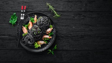 Siyah bir tabak karides ile siyah makarna. Üstten Görünüm. Beyaz ahşap zemin üzerinde. Ücretsiz kopya alanı.