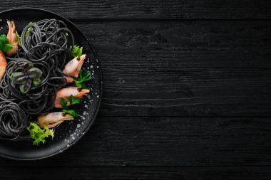 Siyah bir tabak karides ile siyah makarna. Üstten Görünüm. Beyaz ahşap zemin üzerinde. Ücretsiz kopya alanı.