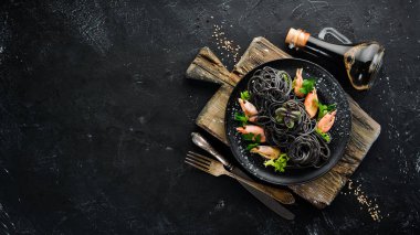 Siyah bir tabak karides ile siyah makarna. Üstten Görünüm. Beyaz ahşap zemin üzerinde. Ücretsiz kopya alanı.