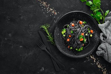 Siyah bir tabakta sebze ile siyah makarna. Üstten Görünüm. Beyaz ahşap zemin üzerinde. Ücretsiz kopya alanı