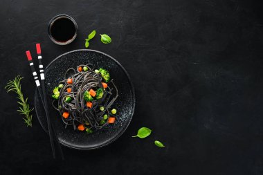 Siyah bir tabakta sebze ile siyah makarna. Üstten Görünüm. Beyaz ahşap zemin üzerinde. Ücretsiz kopya alanı