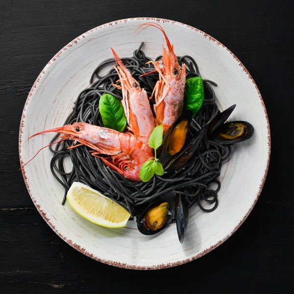 Black spaghetti. Black pastas with seafood and lemon. Shrimp and mussels. On the old background. Top view. Free space for your text.