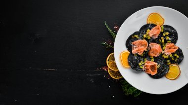 Siyah ravioli somon ve parmesan peyniri ile. Tabağa ahşap arka plan. Üstten Görünüm. Ücretsiz kopya alanı.