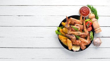 Patates ve sebzeler üzerinde beyaz bir arka plan ile pişmiş tavuk kanatları. Et. Üstten Görünüm. Ücretsiz kopya alanı.