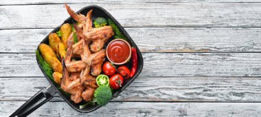 Patates ve sebzeler üzerinde beyaz bir arka plan ile pişmiş tavuk kanatları. Et. Üstten Görünüm. Ücretsiz kopya alanı.