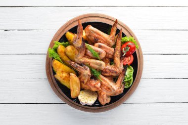 Patates ve sebzeler üzerinde beyaz bir arka plan ile pişmiş tavuk kanatları. Et. Üstten Görünüm. Ücretsiz kopya alanı.