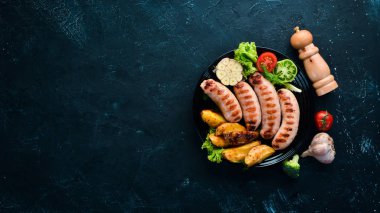 Patates ve sebze siyah taş zemin ile ızgara sosis. Et. Üstten Görünüm. Ücretsiz kopya alanı.