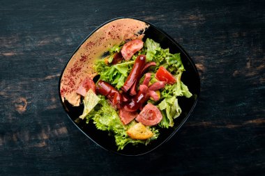 Salata taze sebze ve sosis siyah bir tabak içinde. Ahşap bir arka plan üzerinde. Üstten Görünüm. Metniniz için boş alan.