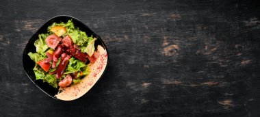 Salata taze sebze ve sosis siyah bir tabak içinde. Ahşap bir arka plan üzerinde. Üstten Görünüm. Metniniz için boş alan.