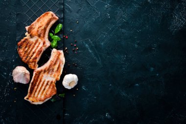 Biberiye ile kemik üzerinde biftekler. Mangal, Barbekü. Siyah taş arka planda. Üst görünüm. Ücretsiz kopya alanı.