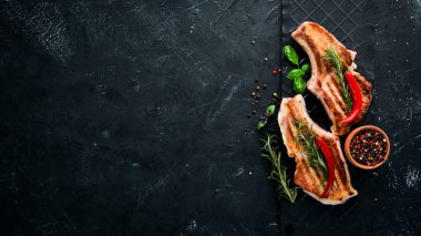 Biberiye ile kemik üzerinde biftekler. Mangal, Barbekü. Siyah taş arka planda. Üst görünüm. Ücretsiz kopya alanı.
