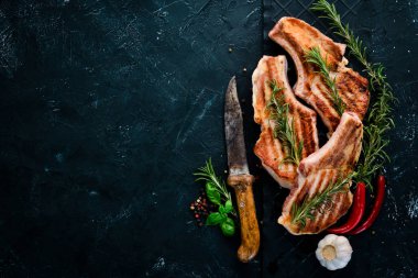 Biberiye ile kemik üzerinde biftekler. Mangal, Barbekü. Siyah taş arka planda. Üst görünüm. Ücretsiz kopya alanı.