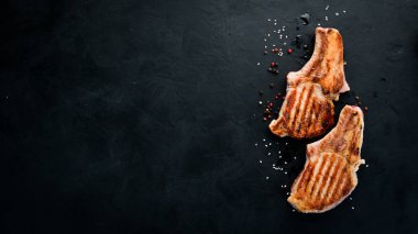 Biberiye ile kemik üzerinde biftekler. Mangal, Barbekü. Siyah taş arka planda. Üst görünüm. Ücretsiz kopya alanı.