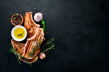 Biberiye ile kemik üzerinde biftekler. Mangal, Barbekü. Siyah taş arka planda. Üst görünüm. Ücretsiz kopya alanı.