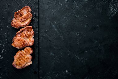 Biberiye ile kemik üzerinde biftekler. Mangal, Barbekü. Siyah taş arka planda. Üst görünüm. Ücretsiz kopya alanı.
