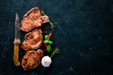 Biberiye ile kemik üzerinde biftekler. Mangal, Barbekü. Siyah taş arka planda. Üst görünüm. Ücretsiz kopya alanı.