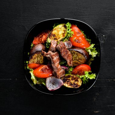 Siyah bir plakada pişmiş sığır eti ve ızgara sebzeler. Ahşap bir arka planda. Üst görünüm. Metniniz için boş alan.