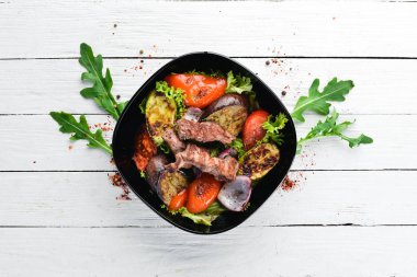 Siyah bir plakada pişmiş sığır eti ve ızgara sebzeler. Ahşap bir arka planda. Üst görünüm. Metniniz için boş alan.