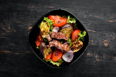 Siyah bir plakada pişmiş sığır eti ve ızgara sebzeler. Ahşap bir arka planda. Üst görünüm. Metniniz için boş alan.