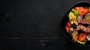 Siyah bir plakada pişmiş sığır eti ve ızgara sebzeler. Ahşap bir arka planda. Üst görünüm. Metniniz için boş alan.