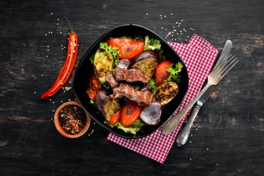 Siyah bir plakada pişmiş sığır eti ve ızgara sebzeler. Ahşap bir arka planda. Üst görünüm. Metniniz için boş alan.