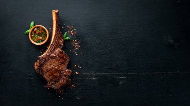 Steak on the bone. tomahawk steak On a black wooden background. Top view. Free copy space. clipart