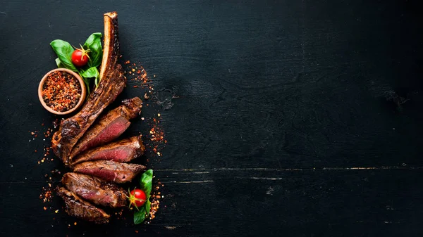 Steak on the bone. tomahawk steak On a black wooden background. Top view. Free copy space.