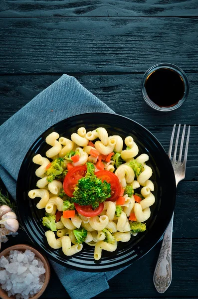 Pasta with vegetables. On a black background. Top view. Free space for your text.