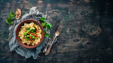 Tabak üzerinde sebze ile farfalle makarna. Üst görünüm. Siyah bir arka planda. Ücretsiz kopya alanı.