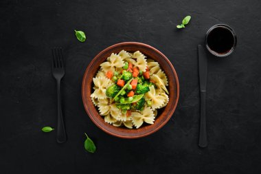 Tabak üzerinde sebze ile farfalle makarna. Üst görünüm. Siyah bir arka planda. Ücretsiz kopya alanı.