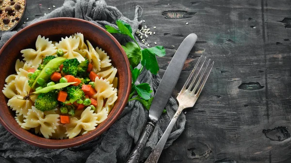 Tabak üzerinde sebze ile farfalle makarna. Üst görünüm. Siyah bir arka planda. Ücretsiz kopya alanı.