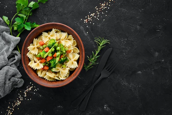 Tabak üzerinde sebze ile farfalle makarna. Üst görünüm. Siyah bir arka planda. Ücretsiz kopya alanı.