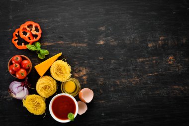 Makarna pişirmek için malzemeler. Kuru makarna. Mantar, sosis, domates, sebze. Üst görünüm. Siyah ahşap bir arka planda. Ücretsiz kopya alanı.