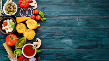 Makarna pişirmek için malzemeler. Kuru makarna. Mantar, sosis, domates, sebze. Üst görünüm. Mavi ahşap bir arka planda. Ücretsiz kopya alanı.